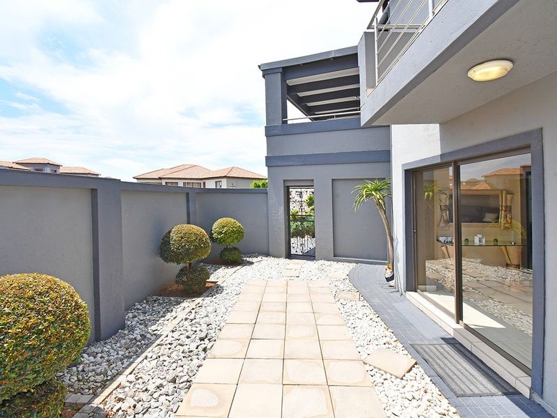A well-maintained rear courtyard featuring a paved walkway, pebble landscaping, and access to the main dwelling via large sliding glass doors.
