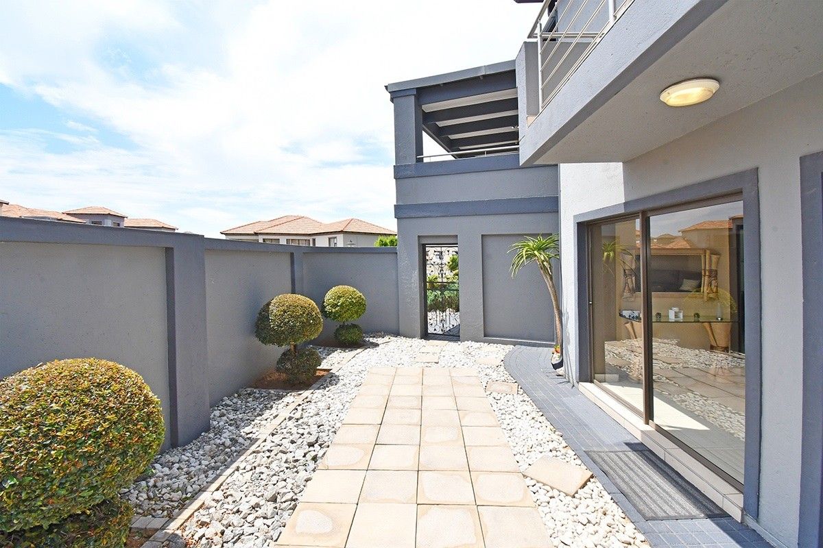 A well-maintained rear courtyard featuring a paved walkway, pebble landscaping, and access to the main dwelling via large sliding glass doors.