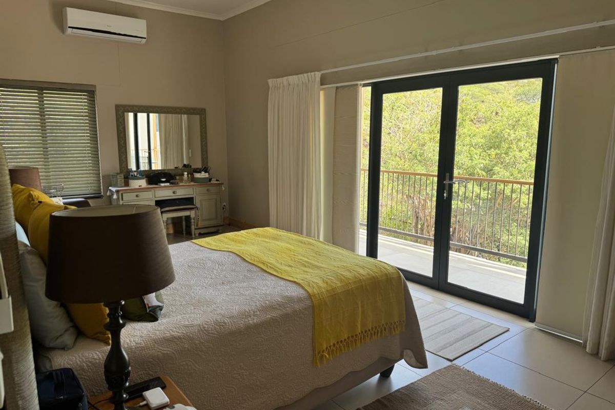 A well-lit bedroom featuring tiled flooring, a wall-mounted air conditioning unit, and large glass sliding doors opening onto a private balcony with scenic views.