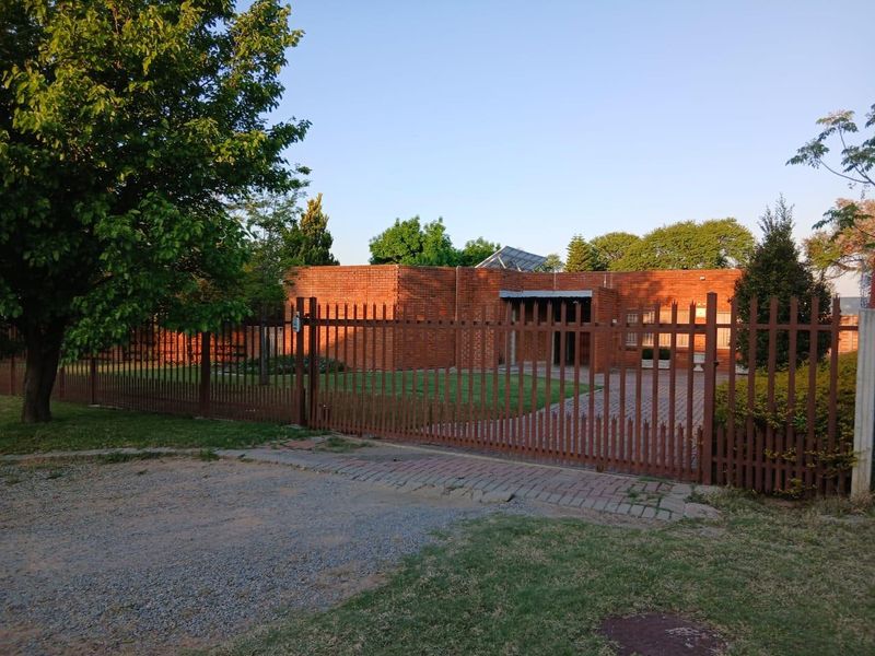 Front view of a face brick house featuring a paved driveway, secure metal perimeter fencing, and solar panels installed on the roof.