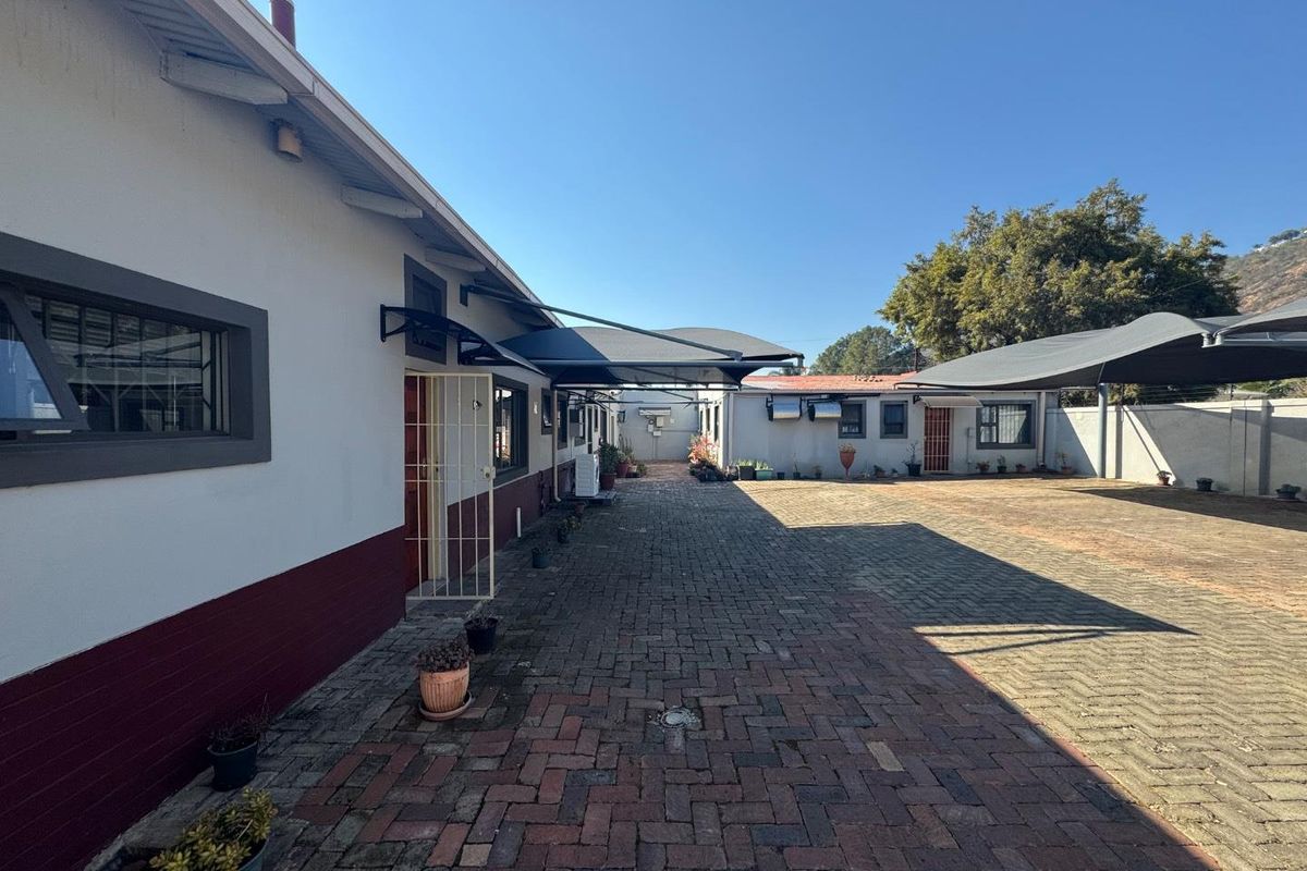 A spacious paved rear courtyard area featuring shade sails, security gates, and access to the main building structure.
