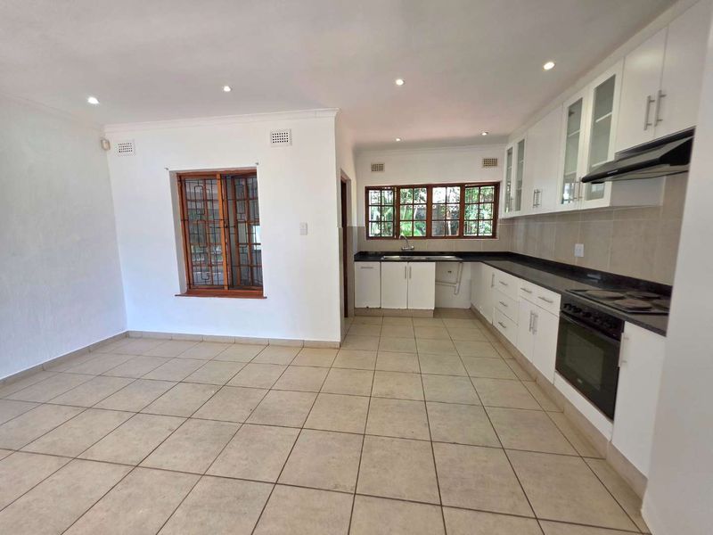 Spacious open-plan kitchen and living area featuring white cabinetry, granite countertops, built-in appliances, and neutral tiled flooring throughout.