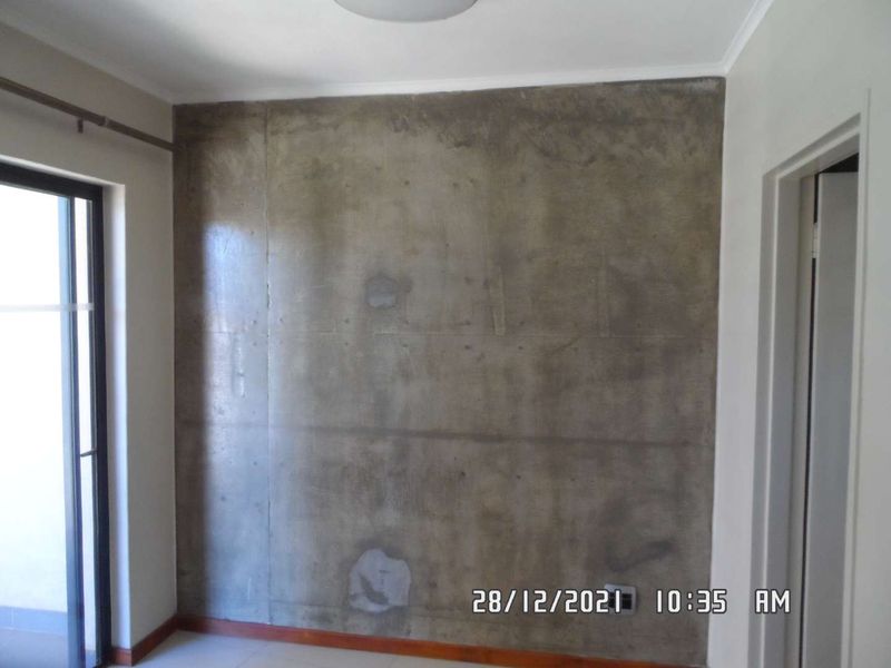 An empty bedroom featuring an exposed concrete feature wall and a sliding glass door leading to an outdoor area.