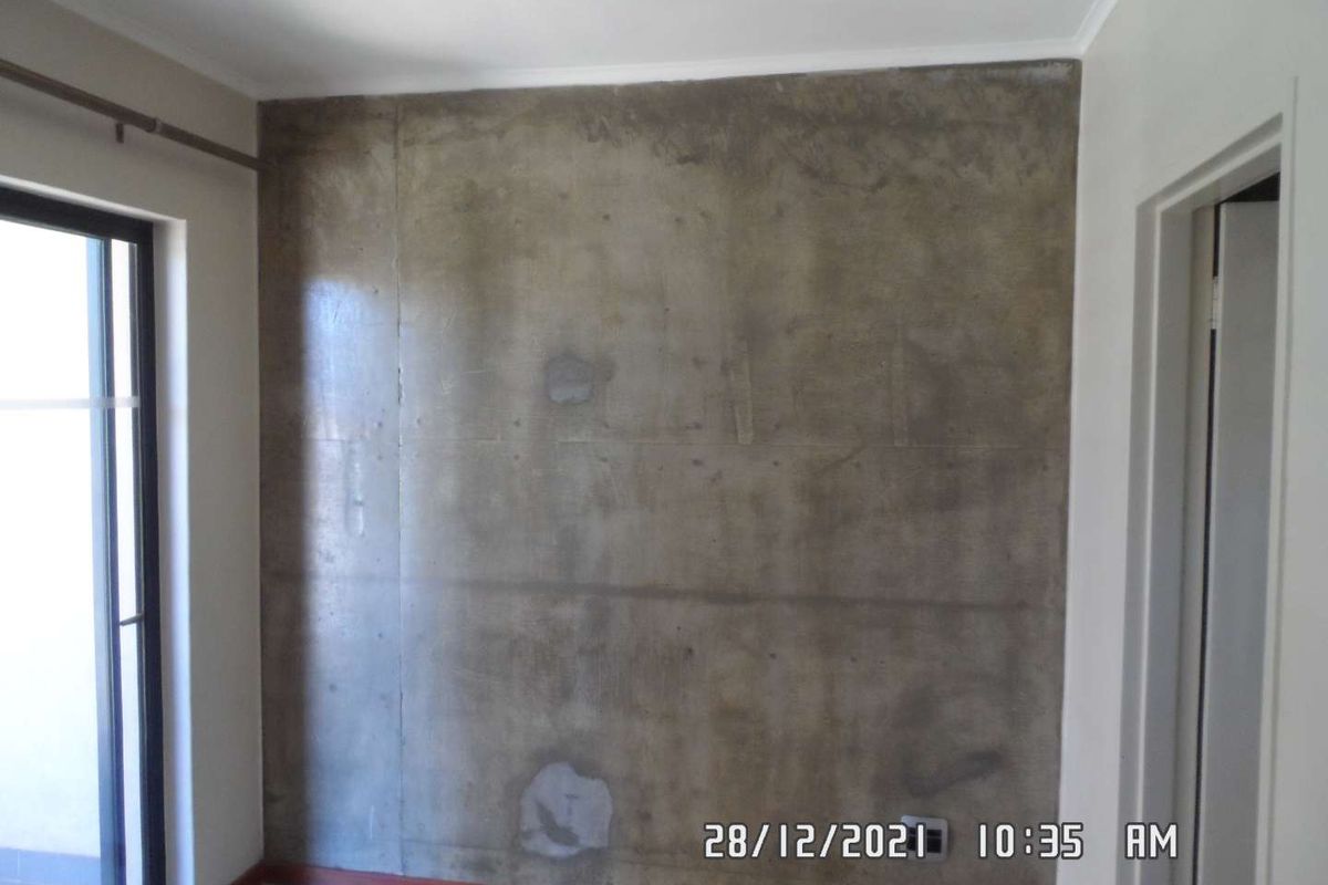 An empty bedroom featuring an exposed concrete feature wall and a sliding glass door leading to an outdoor area.