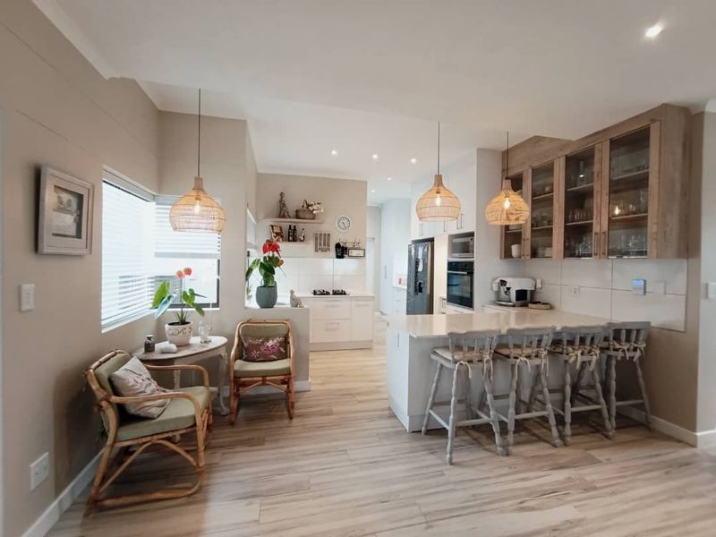 Modern open-plan kitchen featuring a central island with breakfast bar seating, sleek cabinetry, stone countertops, and integrated appliances, finished with contemporary lighting and flooring.
