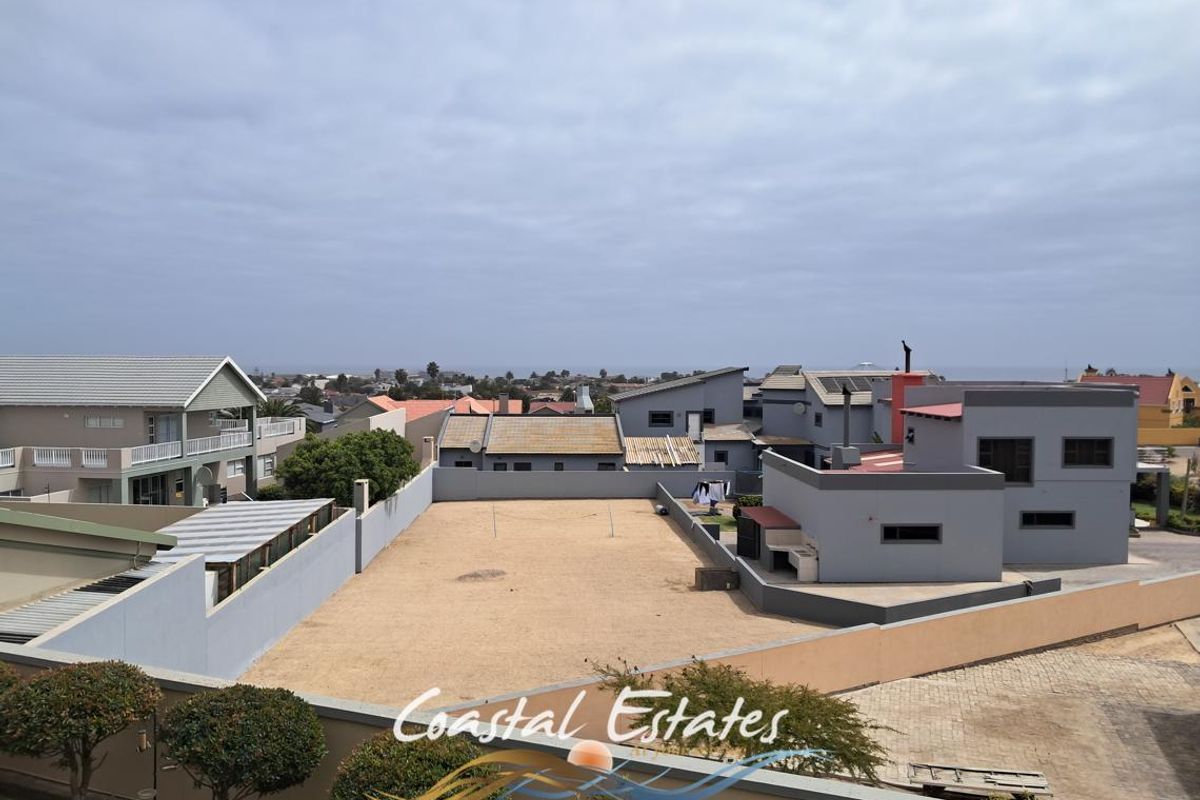 Aerial view of a residential property featuring a large open yard, boundary walls, paved driveway, and a built-in outdoor braai area.