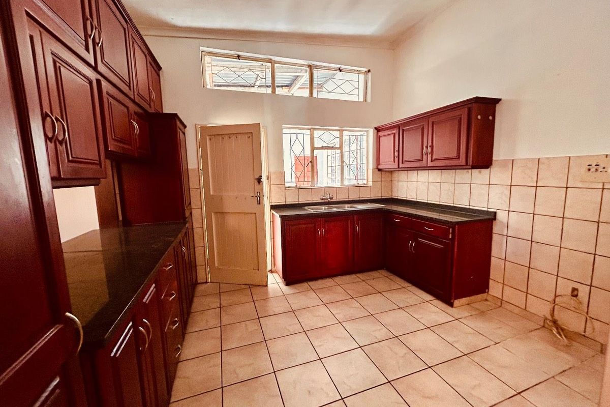 A functional kitchen featuring dark wood cabinetry, granite countertops, tiled flooring, and a double sink with natural light from multiple windows.