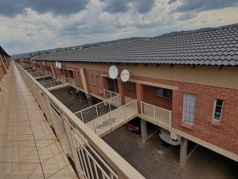 An elevated view of the apartment complex exterior, featuring brick facades, tiled roofing, and a shared walkway overlooking the covered parking area.