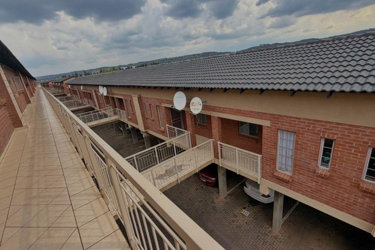 An elevated view of the apartment complex exterior, featuring brick facades, tiled roofing, and a shared walkway overlooking the covered parking area.