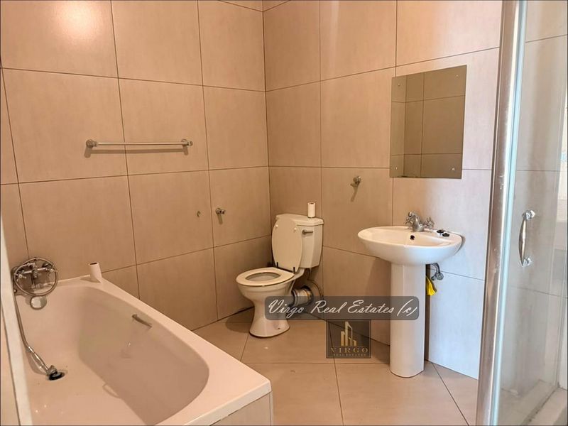 A functional bathroom featuring a pedestal basin, built-in bathtub, separate shower enclosure, and neutral wall tiling throughout.