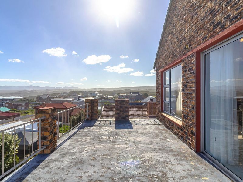 An elevated balcony featuring brick pillars, metal railings, and sliding door access, offering expansive coastal and neighbourhood views.