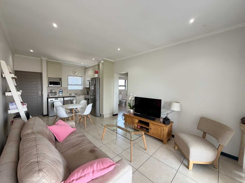 Open-plan living area featuring tiled floors, recessed lighting, and a compact kitchen with built-in cabinetry and appliances, leading to an adjacent bathroom.