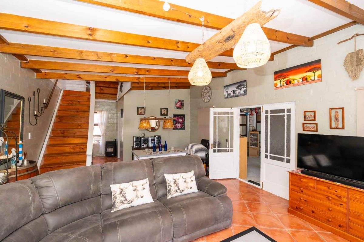 Spacious living room featuring exposed timber ceiling beams, tiled flooring, and a wooden staircase leading to the upper level.