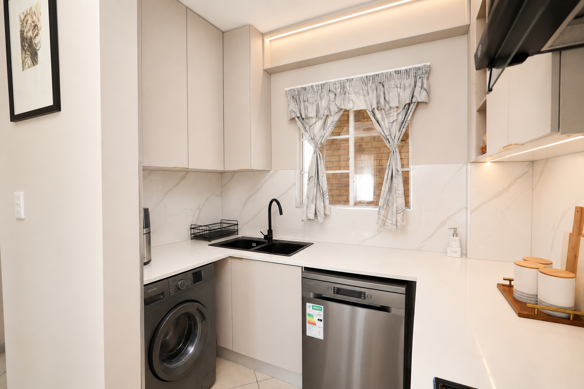 Modern kitchen featuring sleek neutral cabinetry, stone countertops, marble-look splashback, and integrated appliances including a dishwasher and washing machine.