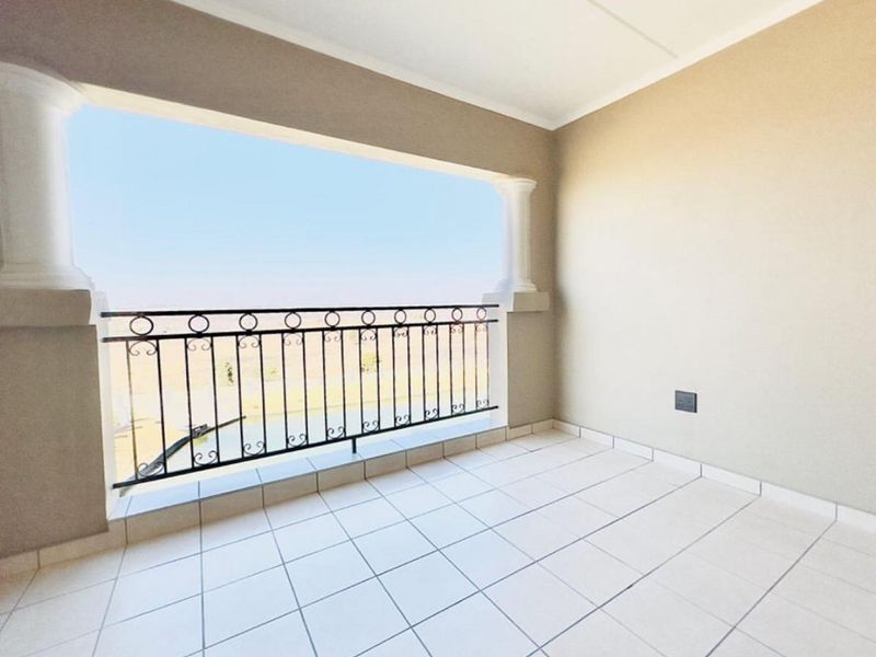 A clean, empty balcony featuring tiled flooring, decorative columns, and a wrought iron balustrade with open views.