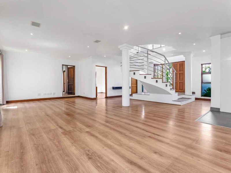 Spacious open-plan living area featuring light wood-look laminate flooring, recessed lighting, and a prominent staircase with a modern stainless steel balustrade.