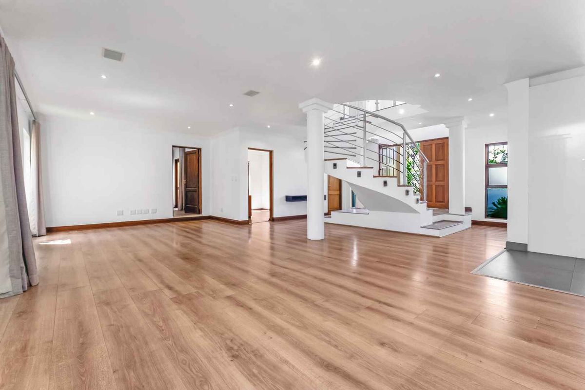 Spacious open-plan living area featuring light wood-look laminate flooring, recessed lighting, and a prominent staircase with a modern stainless steel balustrade.