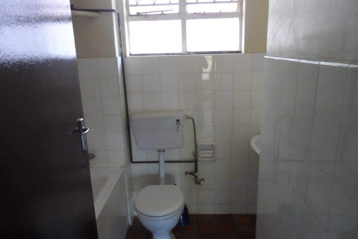 A functional bathroom featuring a standard bathtub, toilet, and washbasin with tiled walls and natural light from a high-set window.