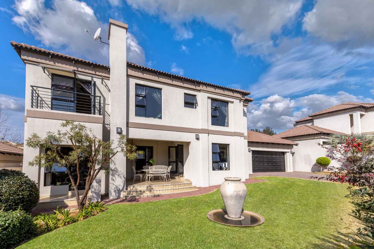 Rear view of a double-story residential property featuring a paved patio, balcony, manicured lawn, and integrated garage.