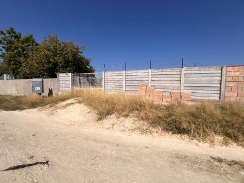 Exterior view of the property boundary featuring a precast concrete wall with razor wire security and an unpaved access road.