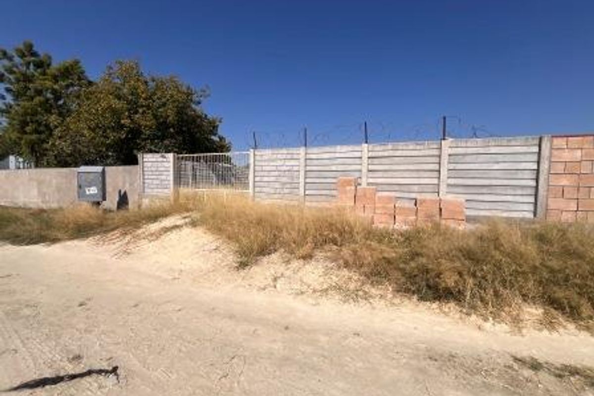 Exterior view of the property boundary featuring a precast concrete wall with razor wire security and an unpaved access road.