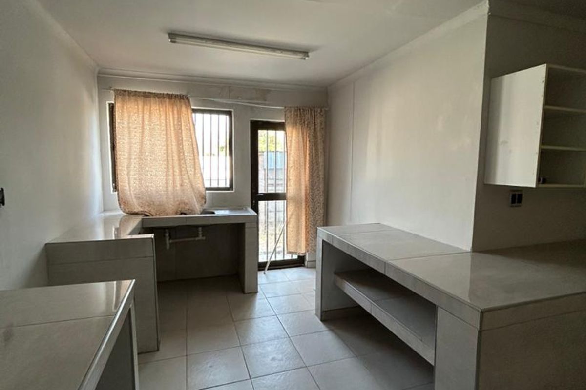 A functional, empty kitchen space featuring tiled countertops, built-in shelving, and ceramic floor tiles, offering a blank canvas for renovation.
