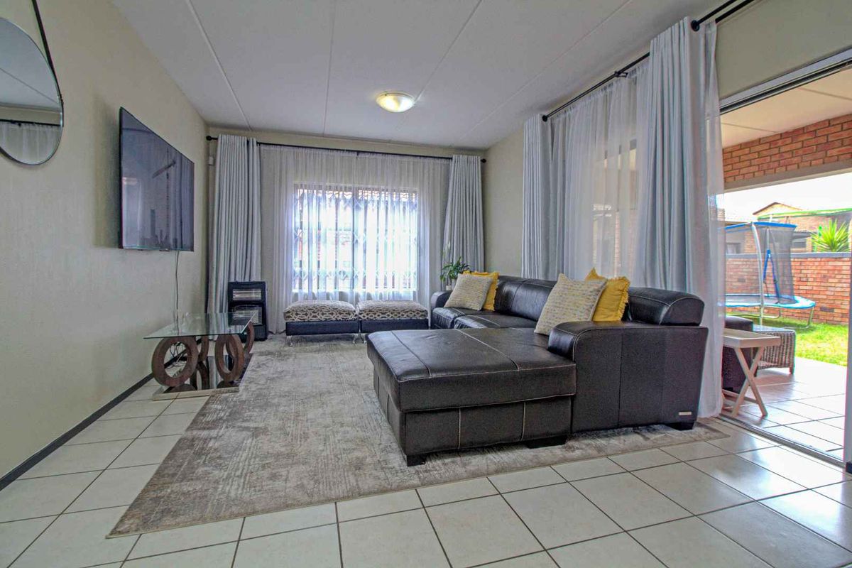 A spacious living room featuring tiled flooring, large windows with curtains, and sliding glass doors providing direct access to an outdoor patio area.