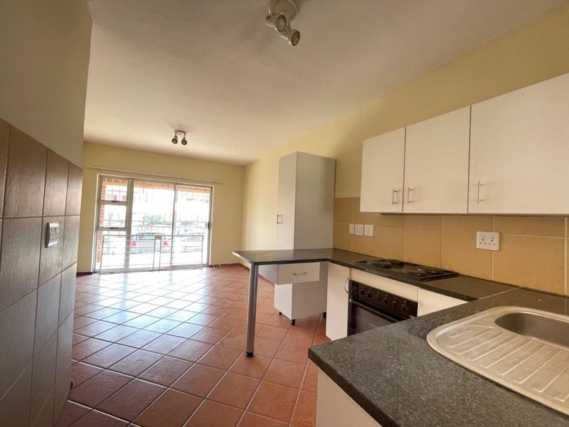 Open-plan kitchen and living area featuring tiled flooring, built-in cabinetry with integrated oven and hob, and a sliding door leading to the exterior.