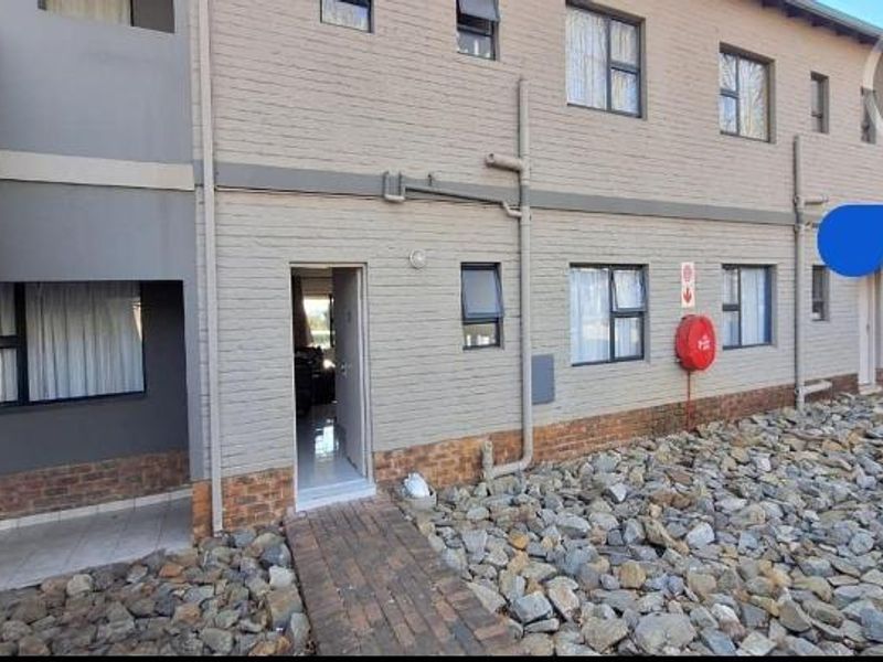 Rear exterior view of a multi-story apartment building featuring brick masonry, paved walkways, and functional fire safety equipment.