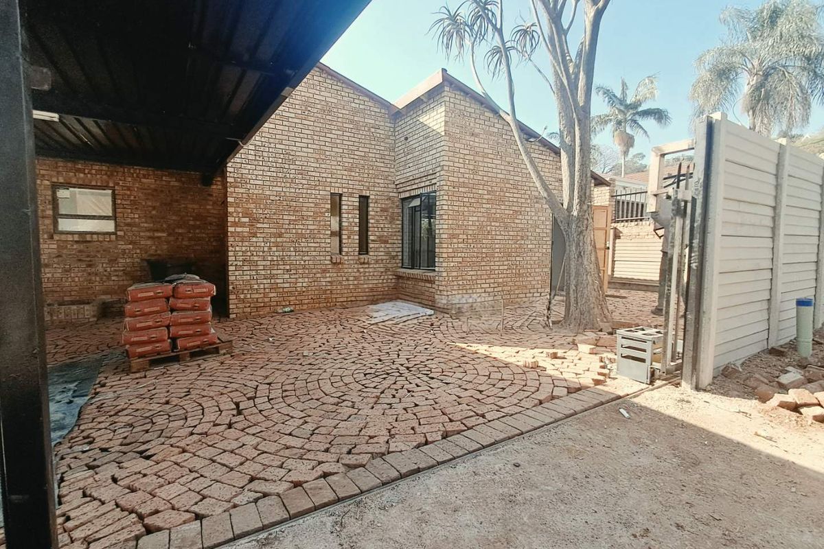 Rear exterior area featuring face brick construction, a covered carport, and ongoing paving installation work in the garden space.