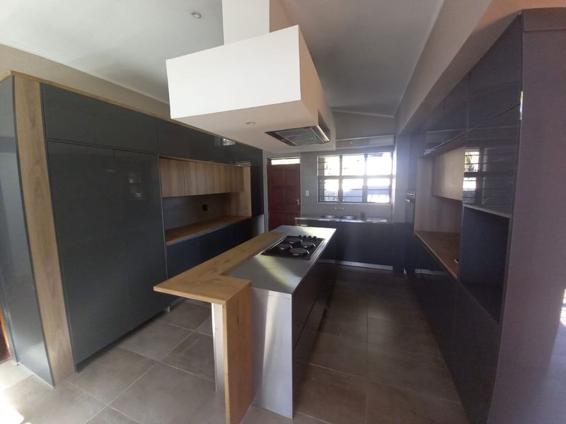 Modern kitchen featuring dark grey cabinetry, a central island with a gas hob, stainless steel countertops, and tiled flooring.
