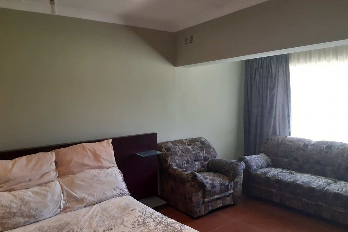 A spacious bedroom featuring tiled flooring, a built-in headboard with integrated shelving, and a large window with curtain tracks.