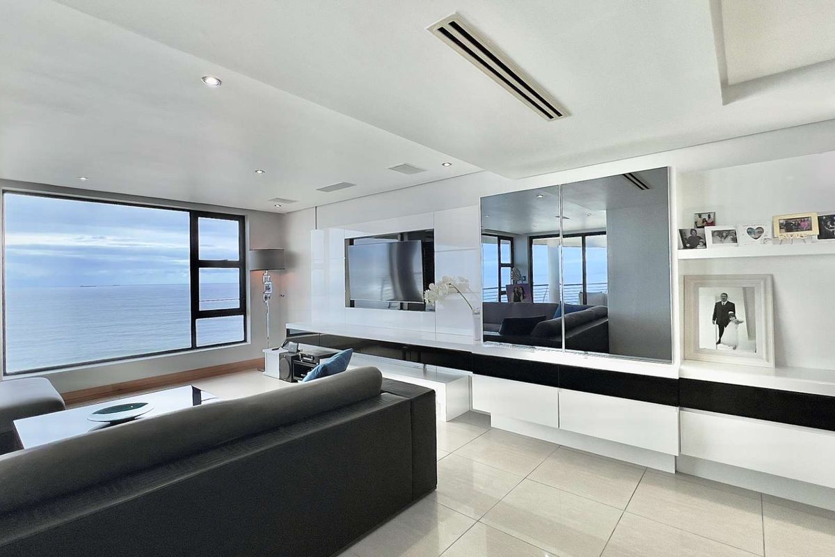 Modern living room featuring high-gloss built-in cabinetry, recessed ceiling lighting, ducted air conditioning, and expansive floor-to-ceiling windows with panoramic ocean views.