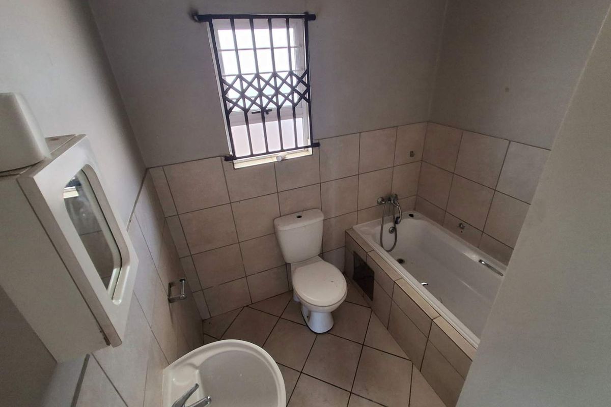 A functional bathroom featuring a bathtub, toilet, and pedestal basin with tiled finishes and security bars on the window.
