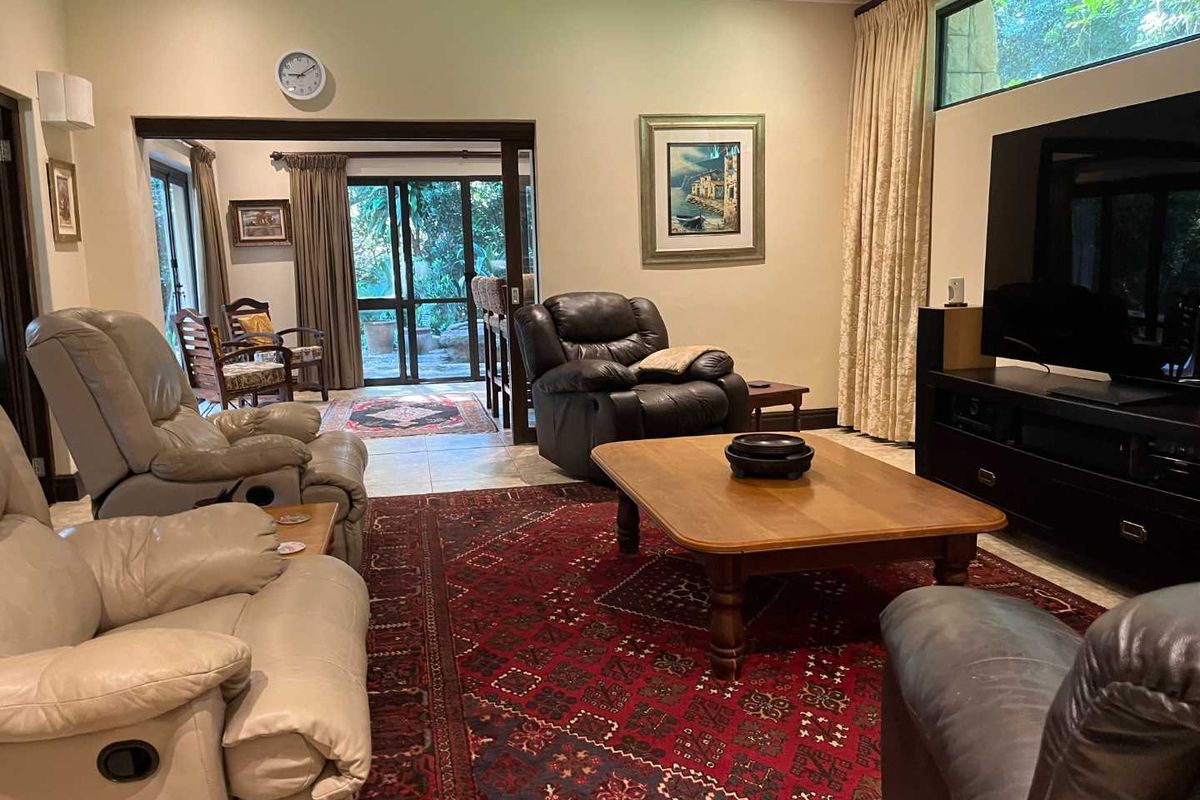 Spacious living room featuring high ceilings, tiled flooring, and large windows, with seamless flow to an adjacent patio area.