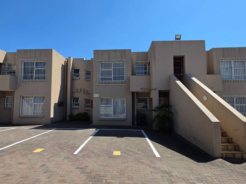 Front elevation of a multi-story townhouse complex featuring paved parking bays, external staircases, and security bars on windows.