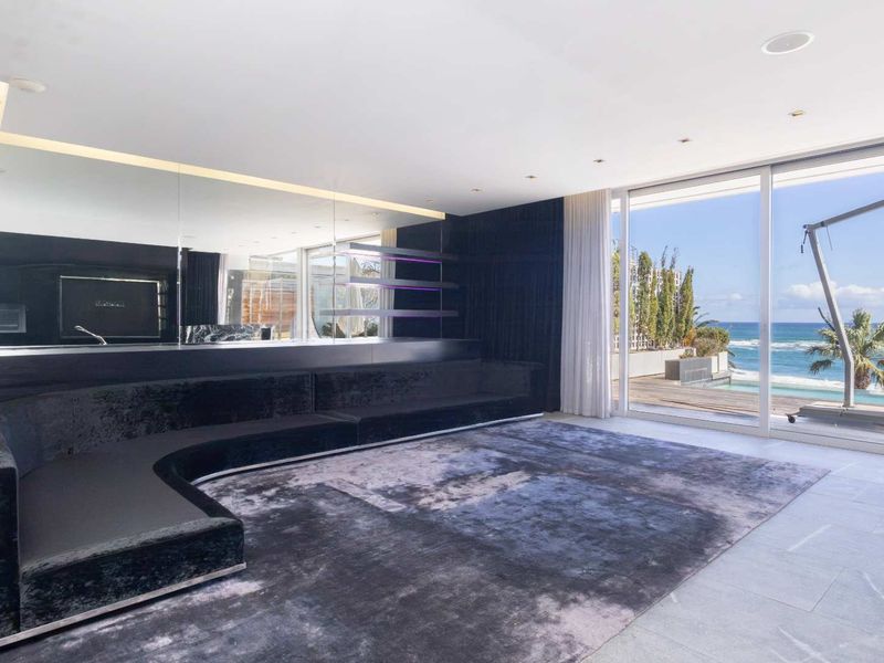 Modern living room featuring built-in curved seating, expansive mirrored walls, and large sliding glass doors opening to a scenic oceanfront patio.