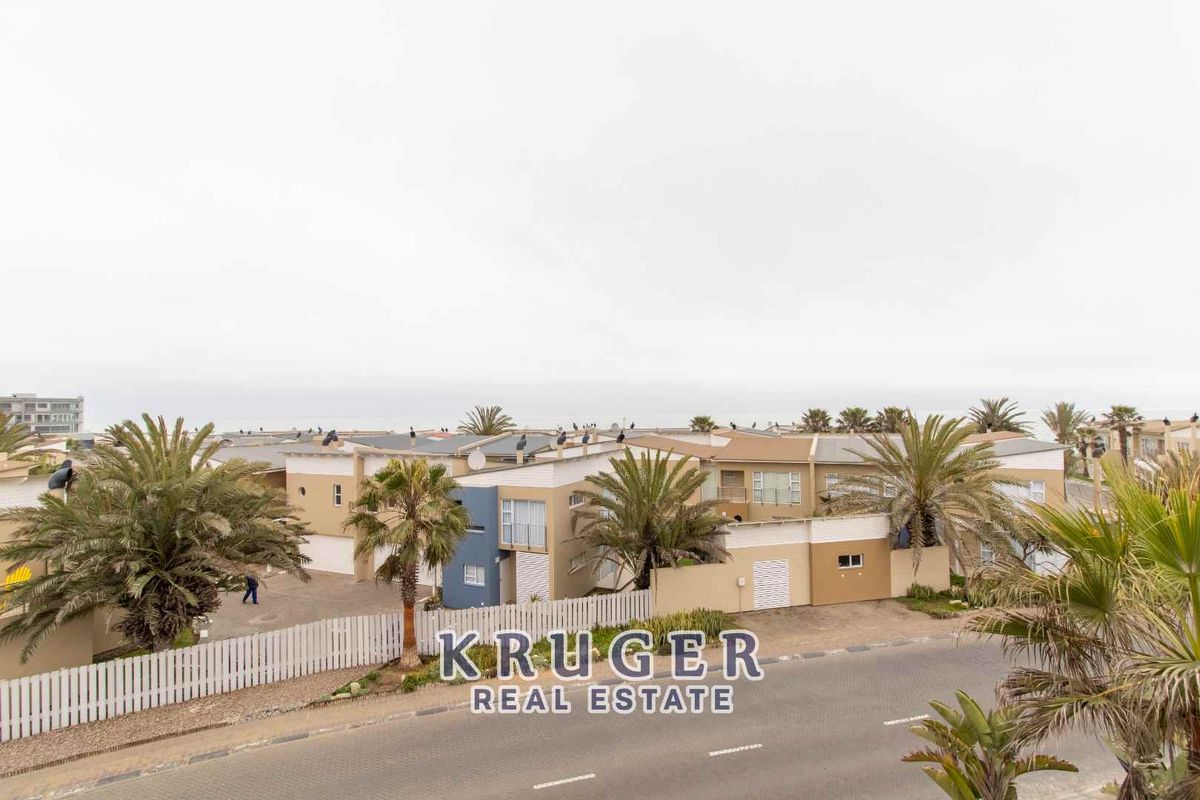 An elevated view of a residential complex featuring modern architectural design, paved driveways, and established palm trees in a coastal setting.