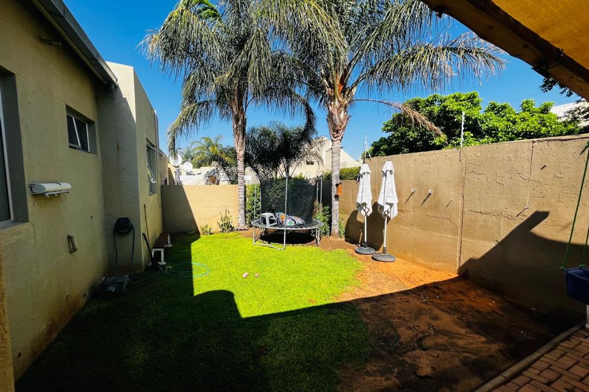 A private rear garden featuring a small lawn, paved patio area, and high boundary walls with electric fencing.