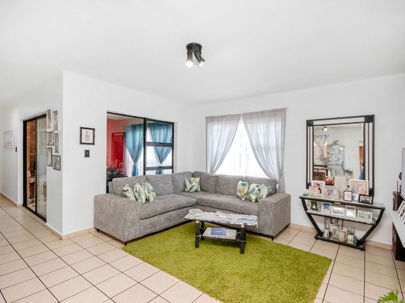 A bright and functional living room featuring tiled flooring, neutral walls, and direct access to an adjacent space through a sliding glass door.