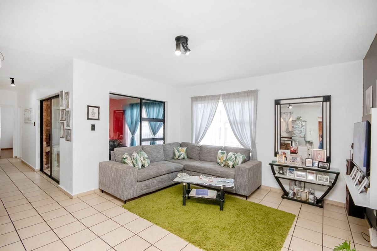 A bright and functional living room featuring tiled flooring, neutral walls, and direct access to an adjacent space through a sliding glass door.