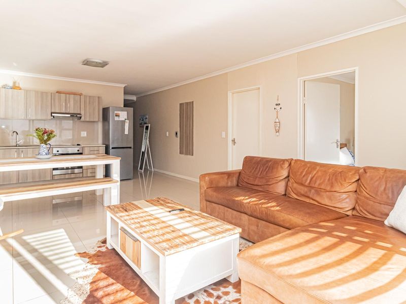 Bright open-plan living area featuring a modern kitchen with built-in cabinetry and tiled flooring, seamlessly flowing into the comfortable lounge space.