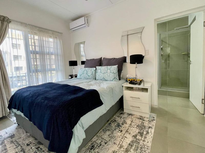 A well-maintained bedroom featuring tiled flooring, an integrated air conditioning unit, and an en-suite bathroom with a glass shower enclosure.