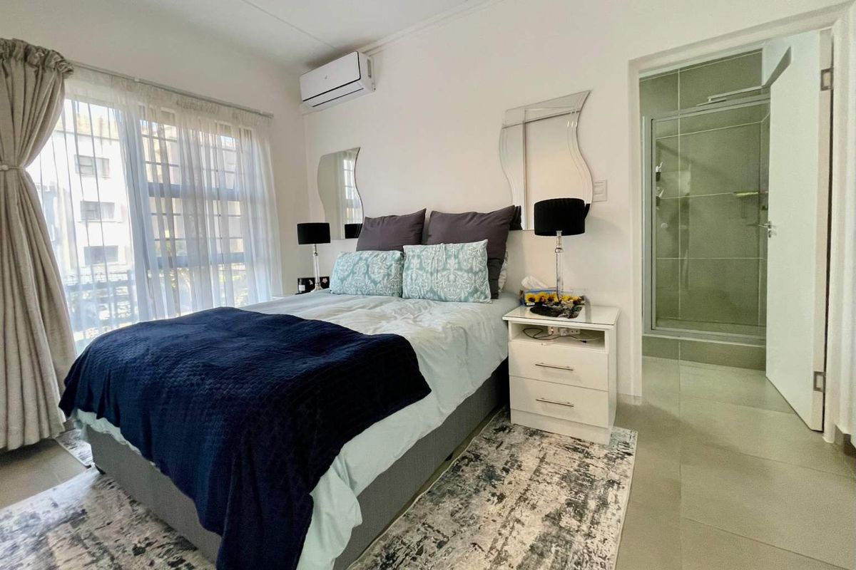 A well-maintained bedroom featuring tiled flooring, an integrated air conditioning unit, and an en-suite bathroom with a glass shower enclosure.