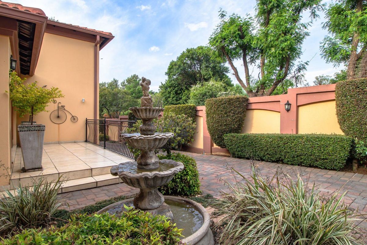 A well-maintained rear garden featuring a tiered stone fountain, paved patio area, and established perimeter hedging.