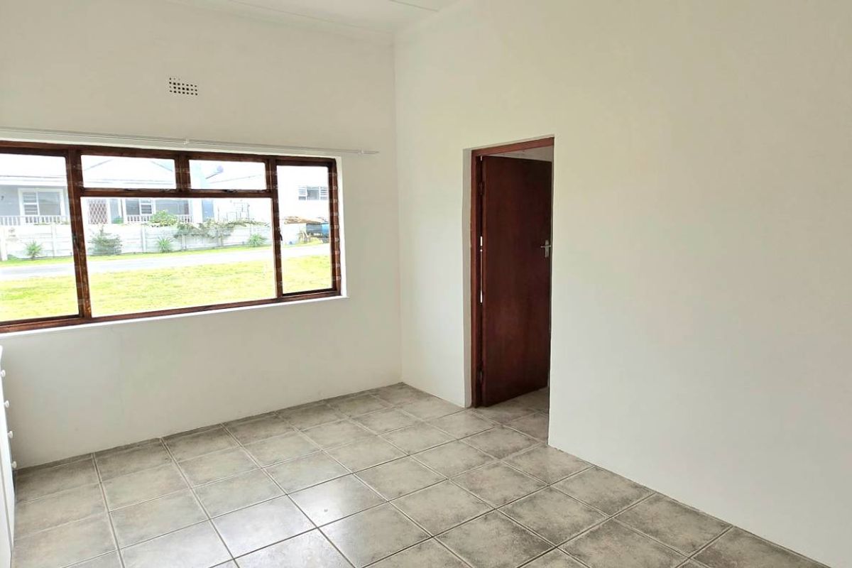 An empty bedroom featuring tiled flooring, built-in cupboards, and a large window providing natural light.