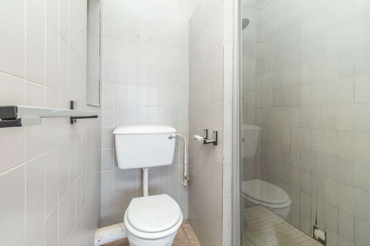 A compact bathroom featuring a standard toilet and a glass-enclosed shower with tiled walls and flooring, requiring some cosmetic updates.