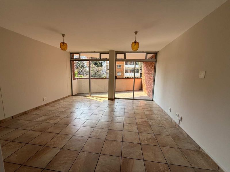 Spacious, empty living area featuring tiled flooring and large sliding glass doors that open onto a private balcony.