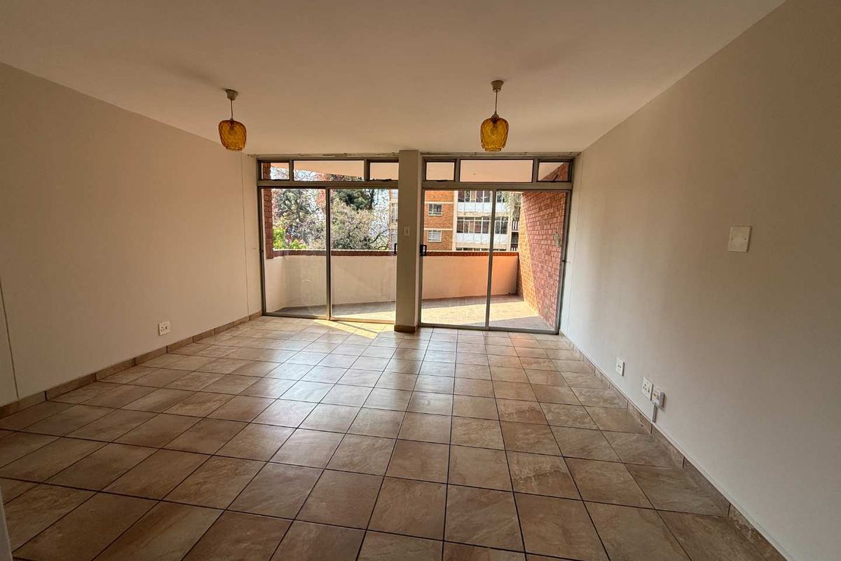 Spacious, empty living area featuring tiled flooring and large sliding glass doors that open onto a private balcony.