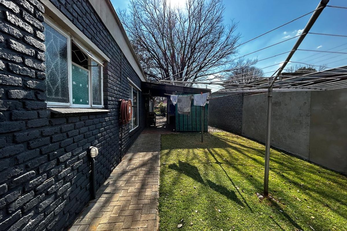 A view of the rear exterior featuring a paved walkway, lawn area, and brick boundary wall along the side of the house.